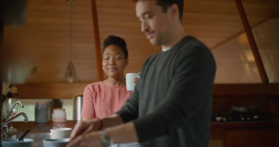 A man and a woman in the kitchen with a man cutting strawberries on a cutting board with a knife