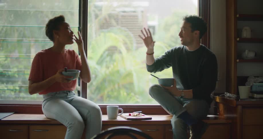 Young happy couple talking and laughing over breakfast in the kitchen at home