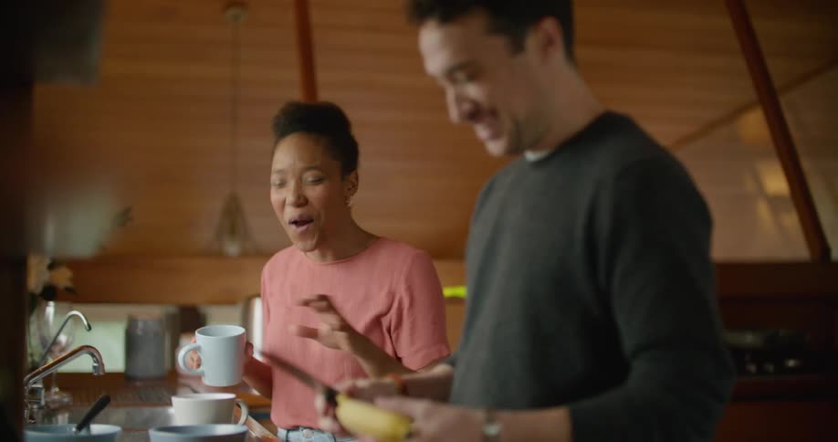 Man and woman talk and laugh as man prepares fruit before feeding strawberry to woman