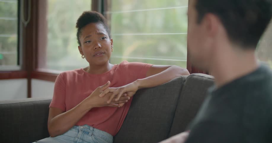 Young couple sitting in the couch at home talking while playing music in a guitar