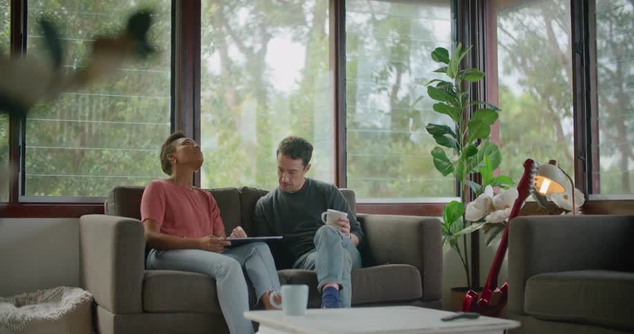 Man and woman sit on sofa sharing use of tablet near red guitar