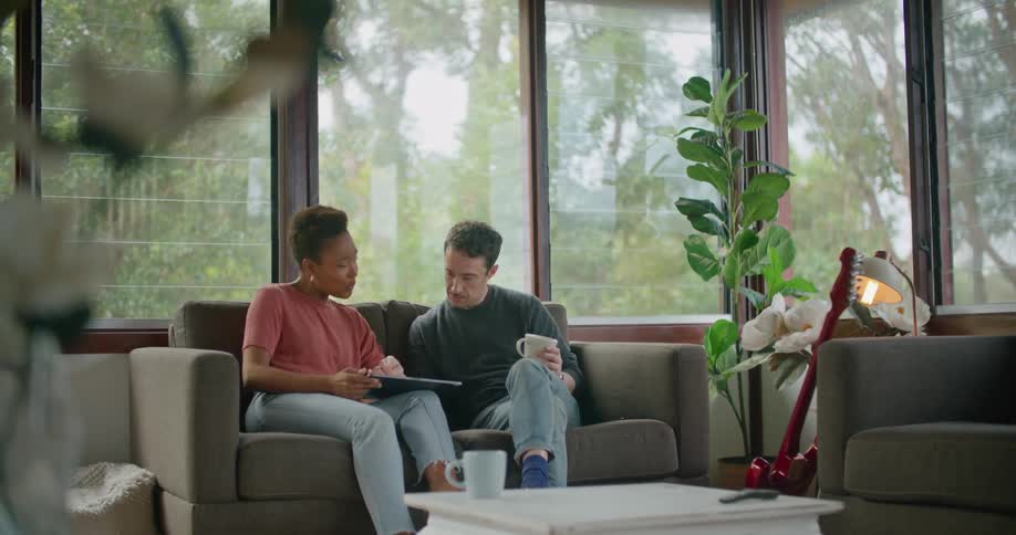 A man and woman sit on a couch looking at a tablet