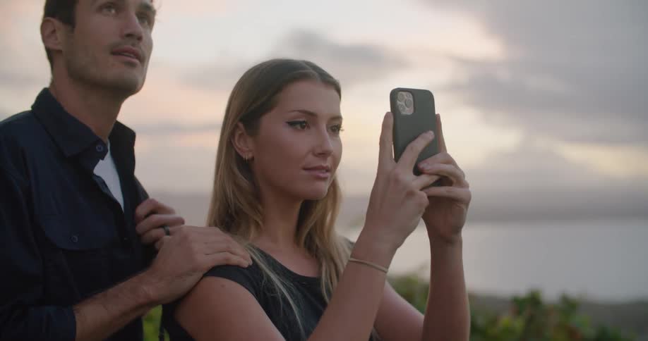 Young couple taking pictures of the landscape at sunset