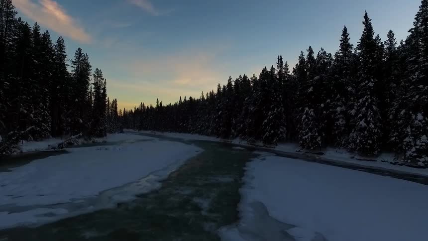 An ice covered stream lined with trees at sunset