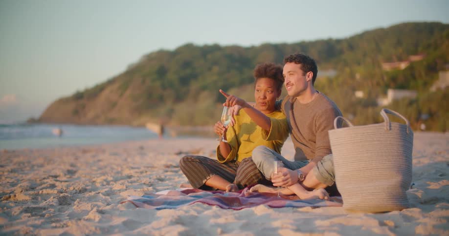 Young happy couple drinking wine while watching the sunset on the beach