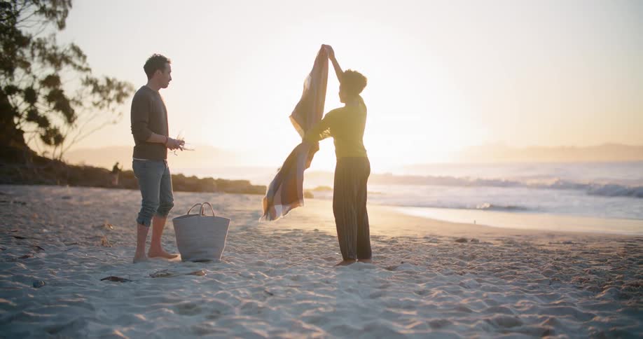 Man and woman lay towel on the beach at sunset by the sea