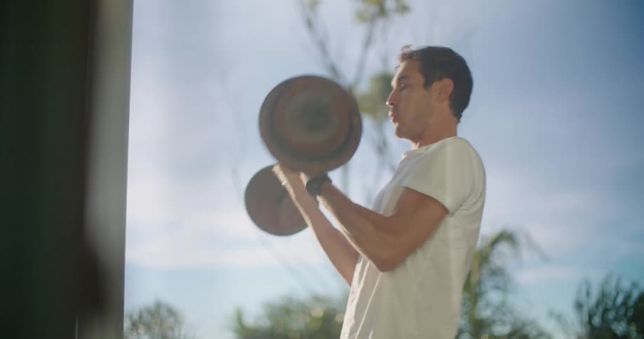 A man lifts a barbell outdoors on a sunny day