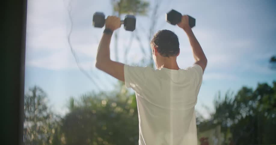 A man exercises using dumbbells on the deck on a sunny day