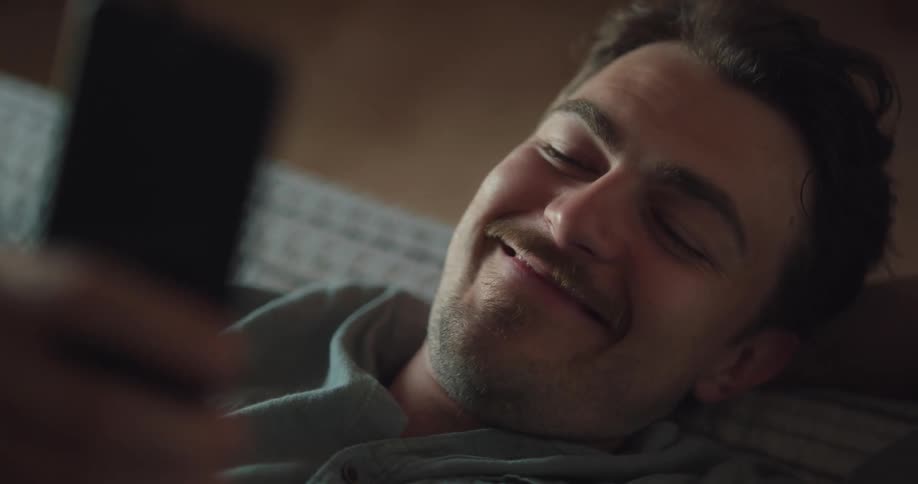 A man laughs while scrolling and typing on his smartphone