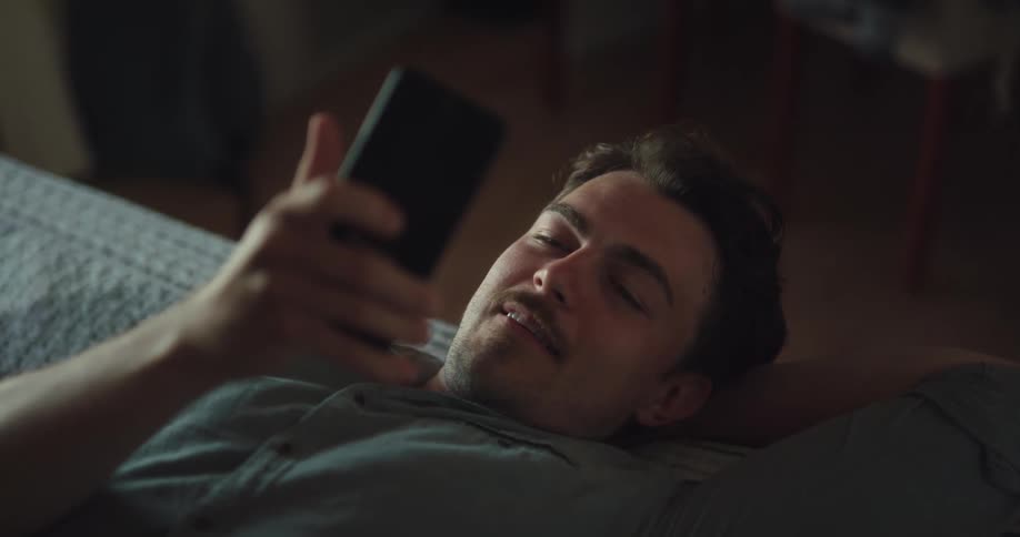 A man smiles and laughs as he scrolls on his cell phone
