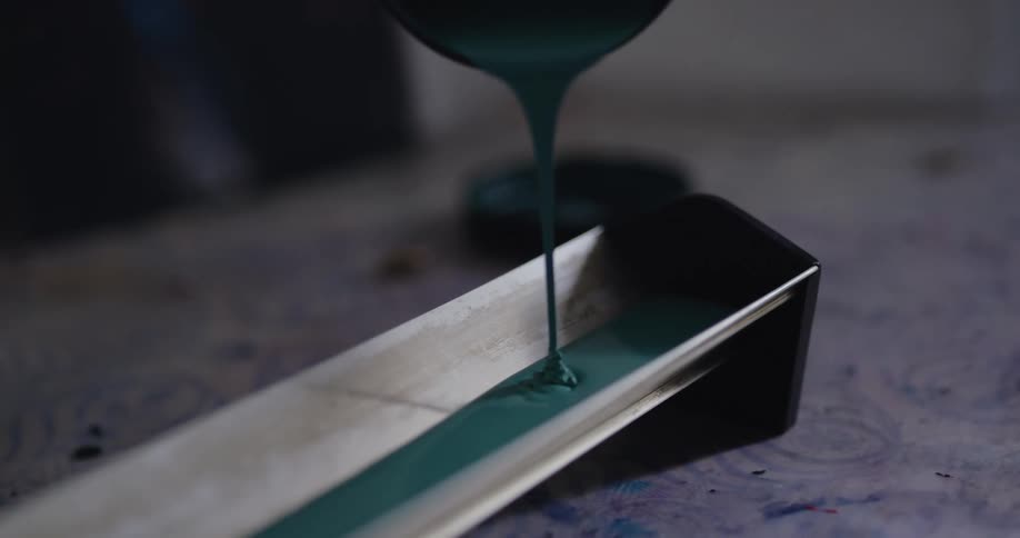 A gloved hand pours ink into the well of a machine