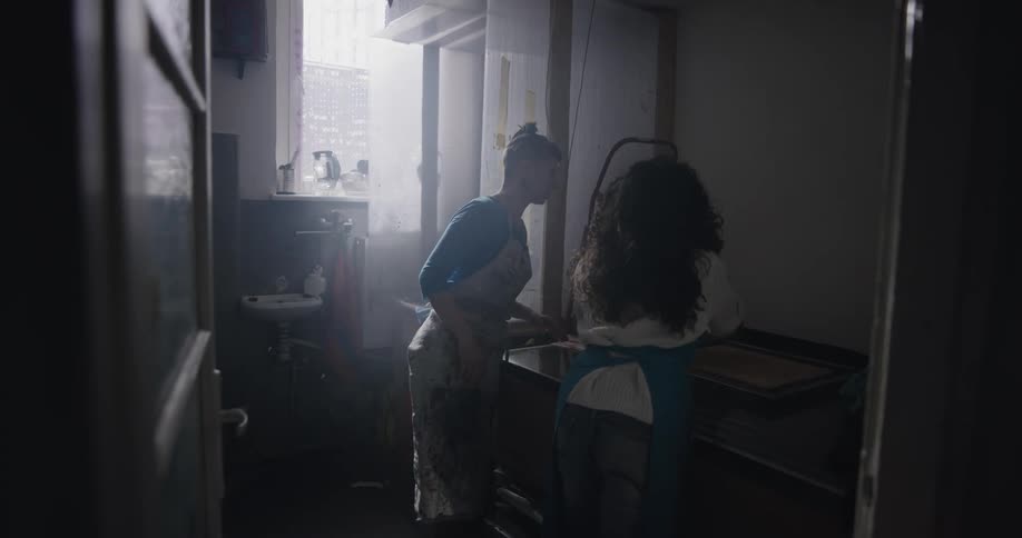 Two women place a large painting on a scanner in the backroom of a business