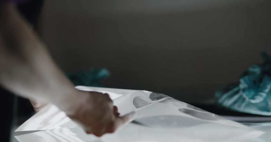 A woman is leaning over an art print and picking it up to touch it