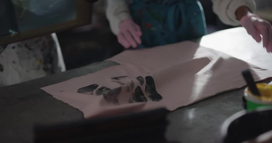 Two people screen print with dark paint onto fabric