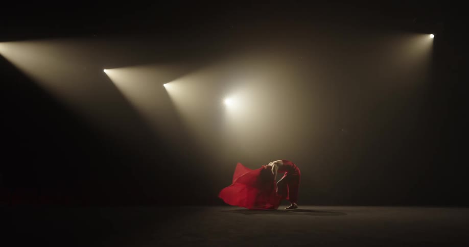 A woman is seen dancing on a smoky stage in a red dress and scarf