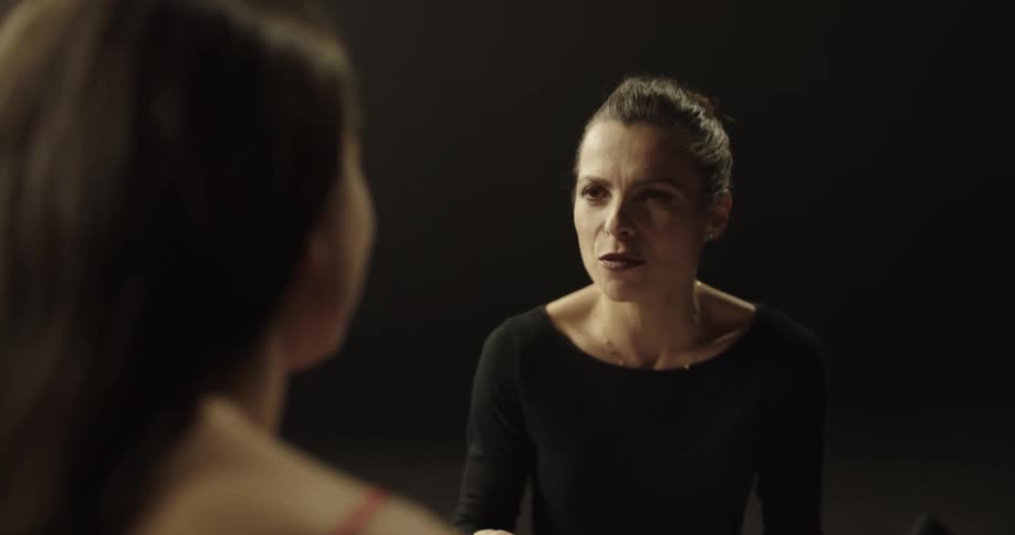 A dance instructor talks with a dancer on a dark stage