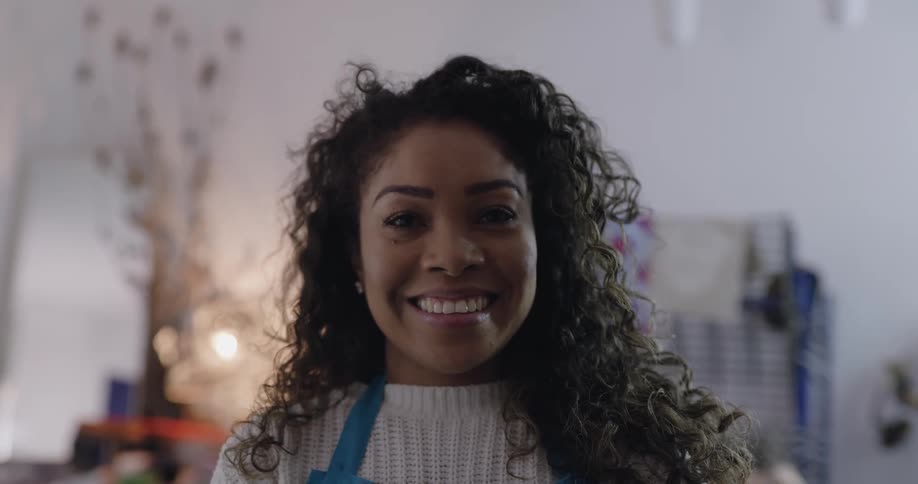 A young woman wearing an apron raisings her eyes to smile into the camera