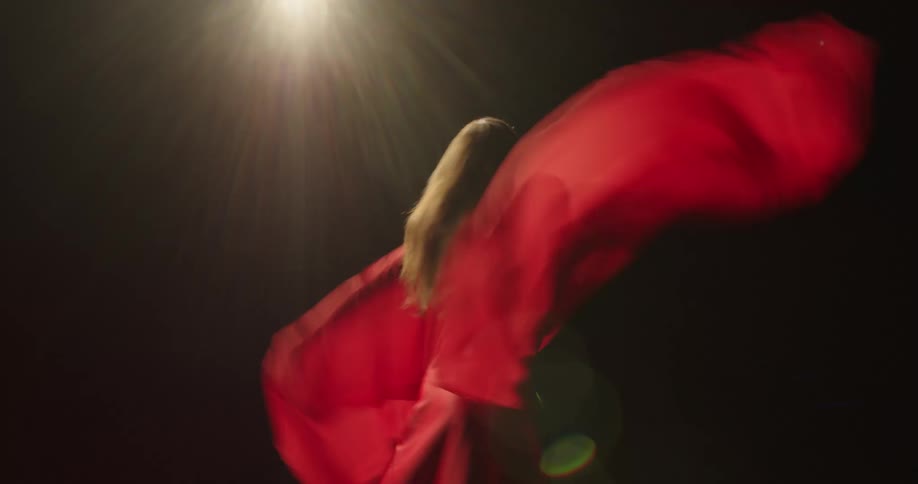 Woman in a red garment spins around while dancing under the bright lights