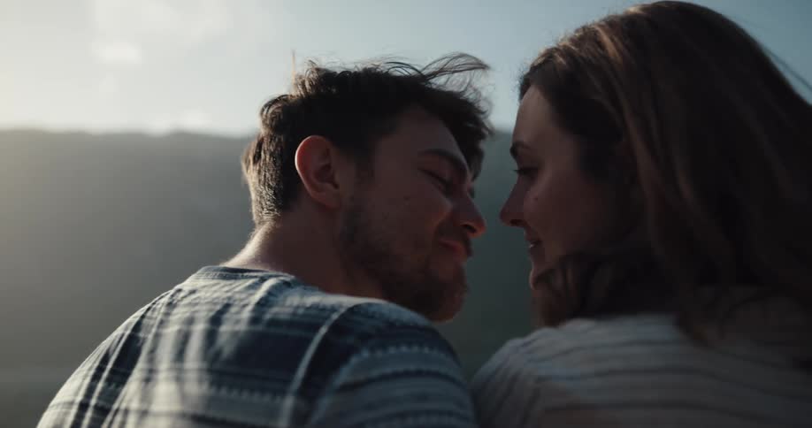 A man and a woman kissing with the sky and clouds in the background