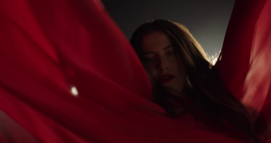 Female dancer wearing red twirls swirling sheer fabric in shadowed room backlit by lights