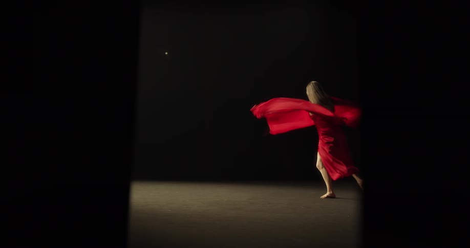 A dancer spins around on stage in a red dress and cape