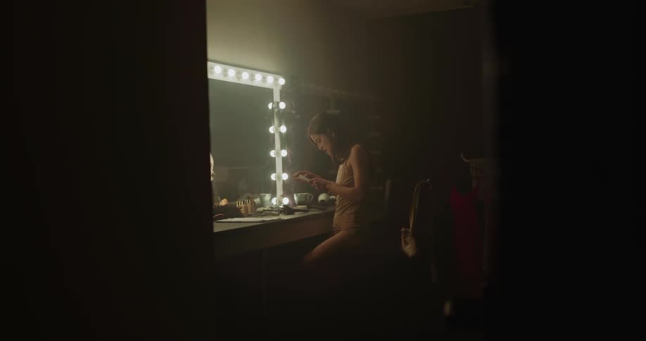 A woman is sitting in front of a mirror as she takes a picture stuck to the mirror and rips it apart