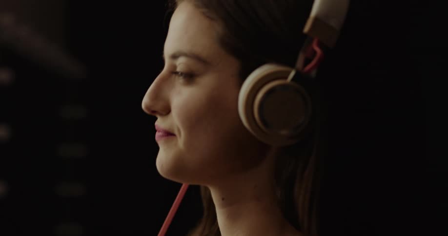 A teenage girl puts headphones on and smiles and moves her head to the music