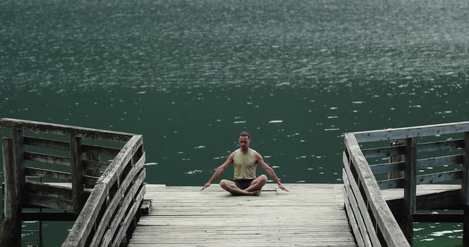 A man is sitting on a dock over the lake and stretching