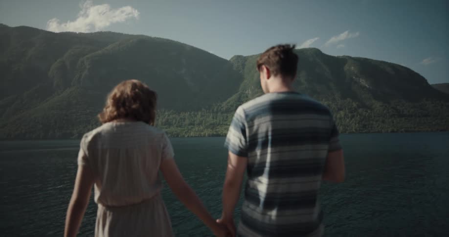 A couple hold hands as they walk along a pier to the edge of a lake