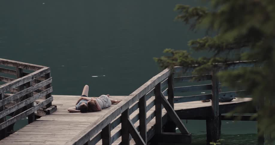 A boyfriend and girlfriend are laying on a dock above the lake