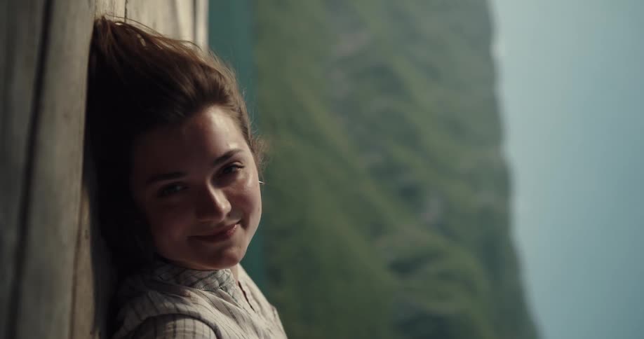 A woman looks at the camera and smiles with lush green mountains visible in the background