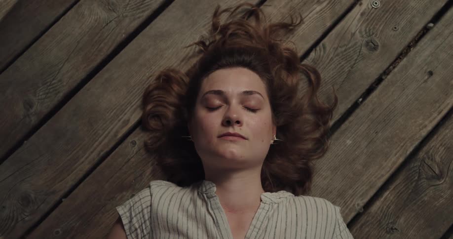 A woman is lying down on wooden floor with her eyes closed