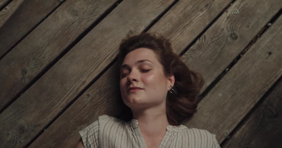 Woman with brown hair hoop earrings and a white shirt lies on pier