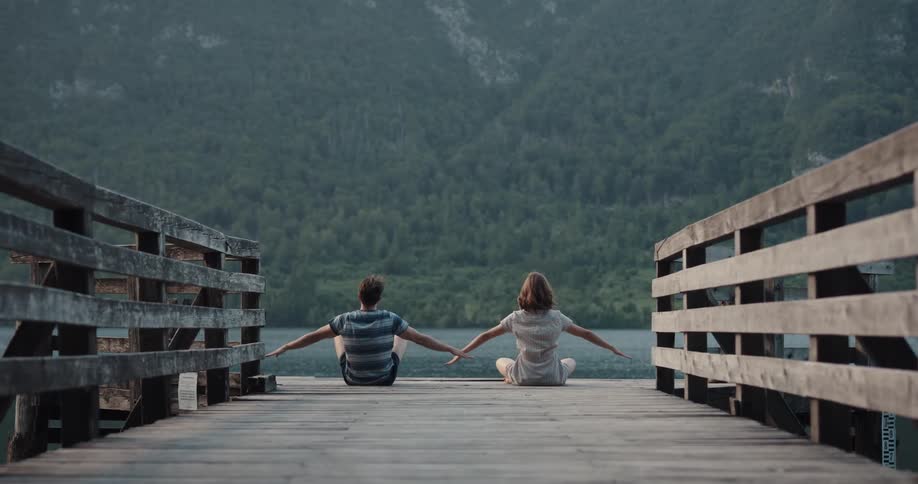 A man and woman are sitting by the lake and stretching