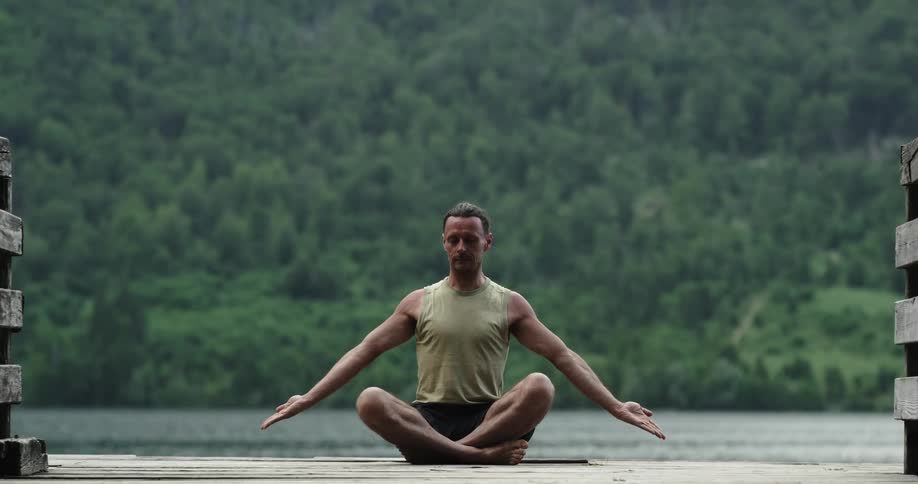 A man sitting on a dock stretching with a river and trees in the background