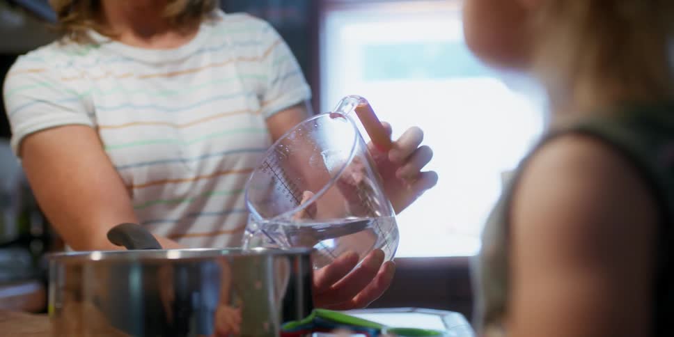 A toddler pours water in a pot as she cooks with her grandma
