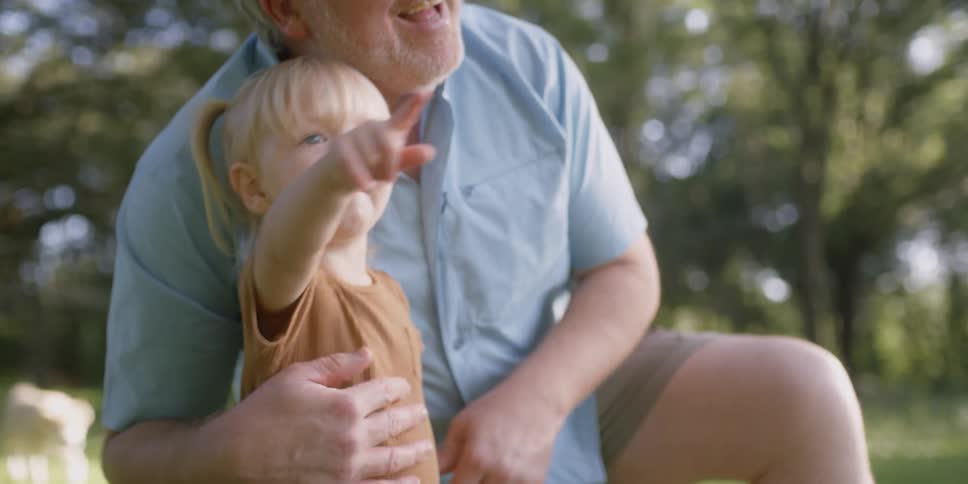 A man kneels to hold a young girl as he points things out to her
