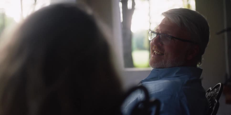 Man wearing glasses sits in a chair and looks over at a woman sitting in a chair next to him