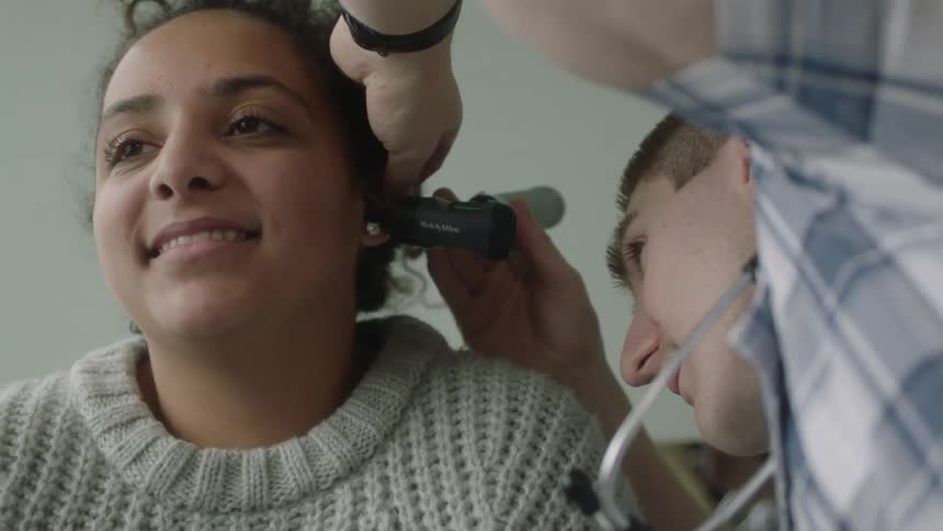 A doctor examines the ear of a woman using a stethoscope