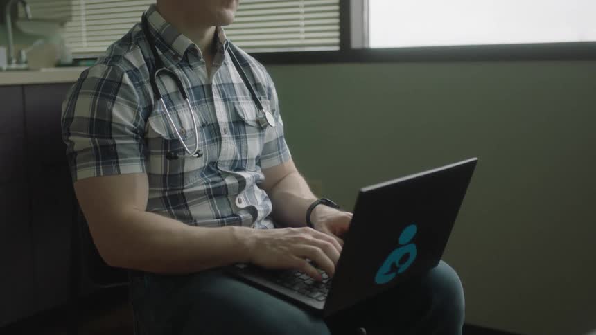 A man is sitting on a chair and typing on a laptop