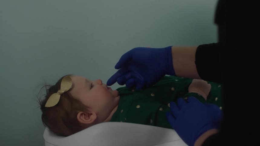 A doctor uses a finger to examine the lips and mouth of a baby girl