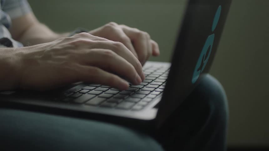 Man with shortsleeved shirt and jeans works on grey laptop