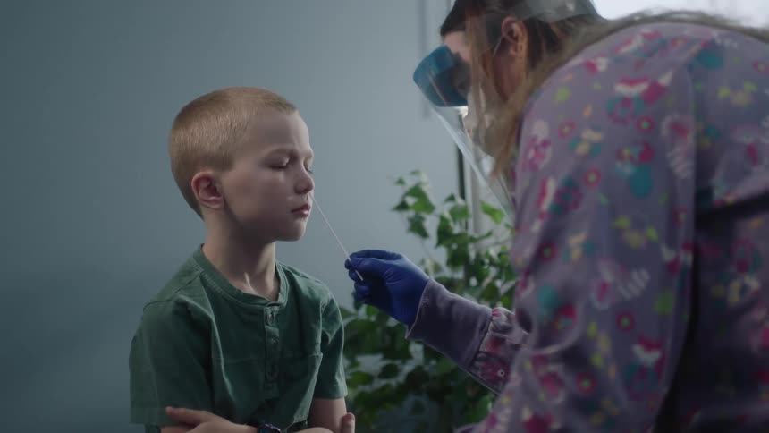 A boy in a clinic with a nurse with gloves putting a cotton swab in his nose