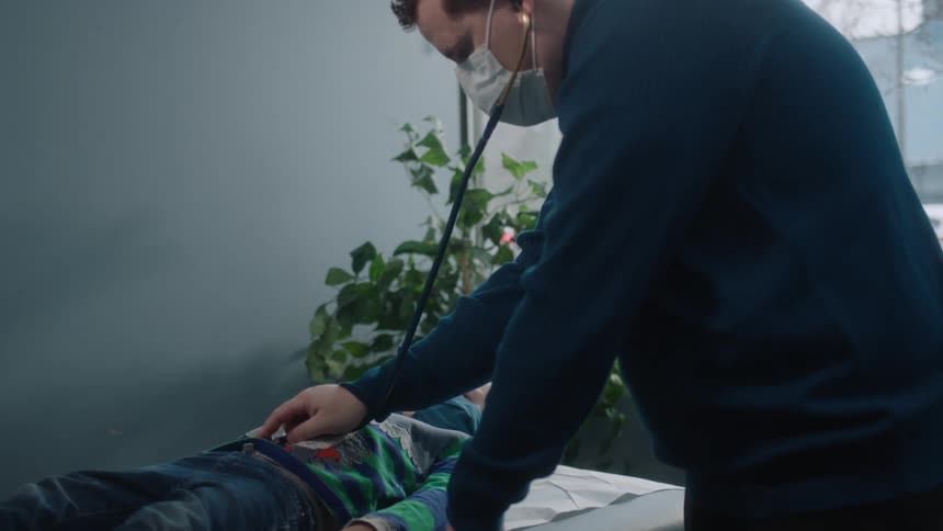 A doctor puts his stethoscope on and leans over a patient to check the heartbeat