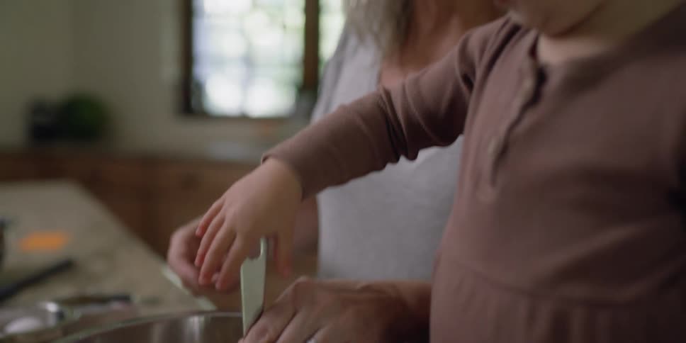 A woman and a child are in a kitchen mixing something in a bowl that is on the counter