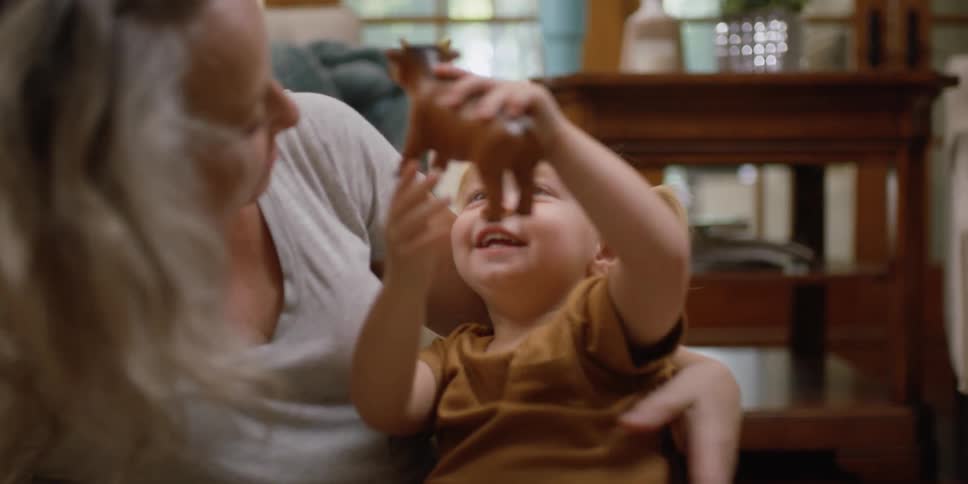 An older female hugs and plays with a smiling little girl who is holding a toy