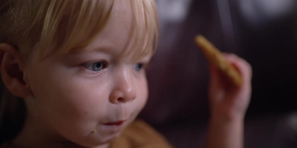 A young girl eats a cookie while sitting on a leather sofa