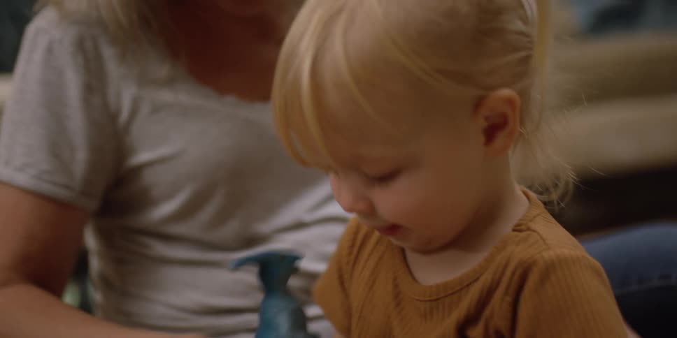 A toddler sits on the floor with her grandmother as they play with plastic animals
