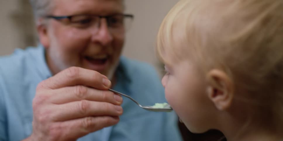 An older man is feeding food to a young boy with a spoon
