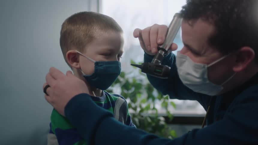 A medical person uses a medical light to look in the ears of a toddler boy